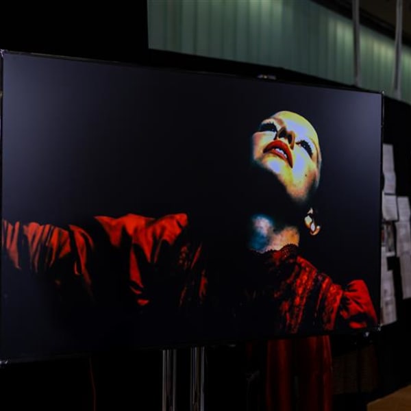 An close-up on a large screen of a person's upturned face and arms stretched out with red sleeves