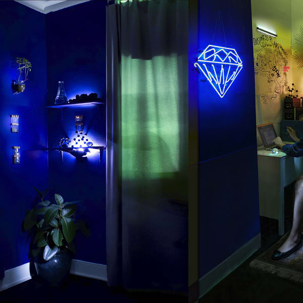 Female working in makeshift lab. Dark blue and neon lighting.