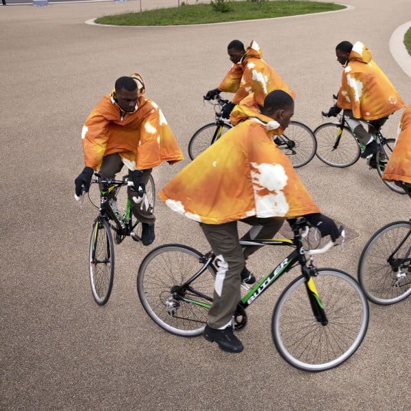 Five black male cyclists wearing orange hoodies.