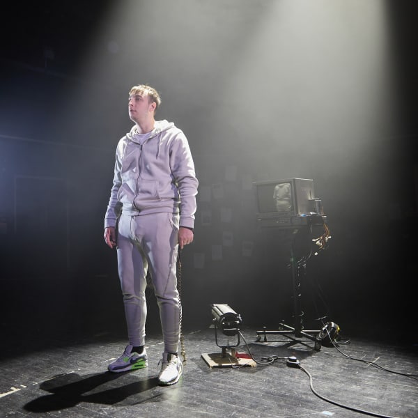 Boy wearing a grey tracksuit and Nike Air Max trainers standing in front of a television monitor.