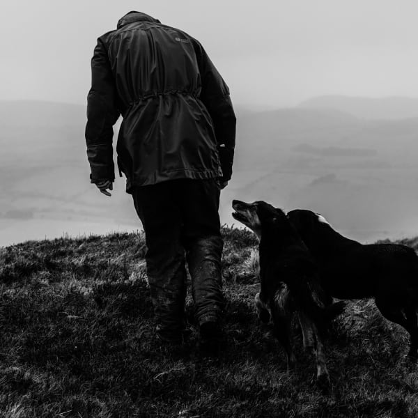 Black and white photograph of a man on a cliff walk with his collie dog.