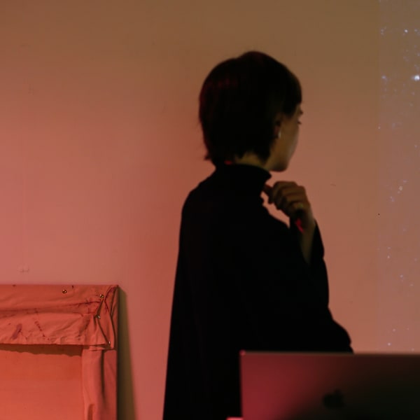 A student is looking at the wall at a piece of artwork which depicts a flower-like projection on the wall with hues of yellow, white and purple