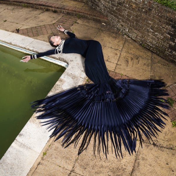 Woman lying across poolside draped in blue spikes dress