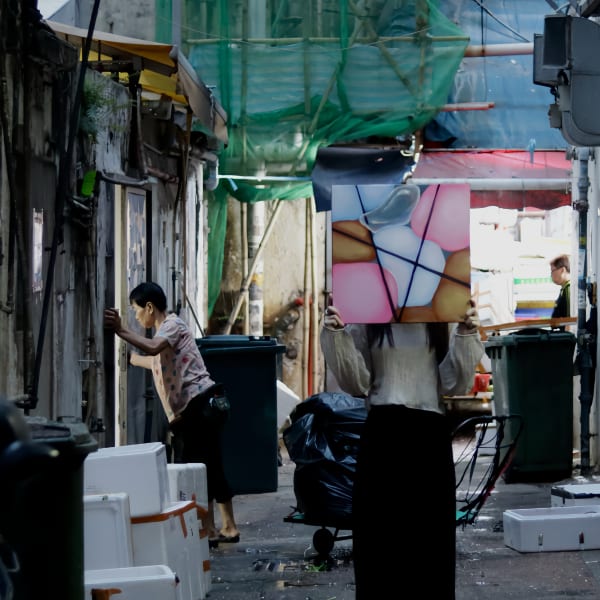 A photo pf a person holding up an artwork in front of their face against the backdrop of an outdoor market
