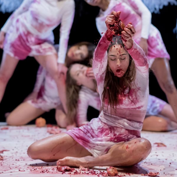 Girls on stage dressed in white crushing pomegranates during a performance of a play called Full Moon.