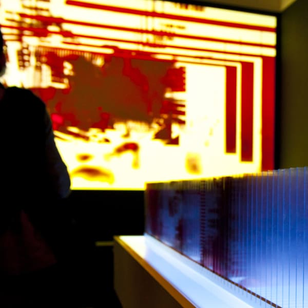 A silhouetted figure stands in front of a red and yellow screen.