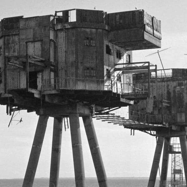 Greyscale photograph of brutalist concrete structures on stilts the water.