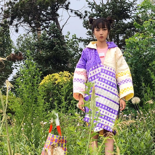 Girl standing amongst grass, tress and bushes wearing a brightly coloured coat.