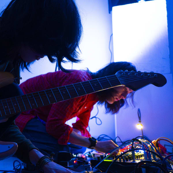 Photo of two students playing guitars in a blue dark light.