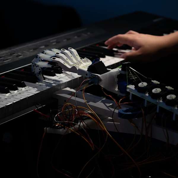 a human hand and a robot hand playing a keyboard