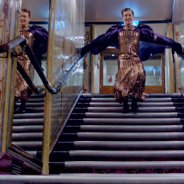 A figure leaps down a staircase within a lavish interior.
