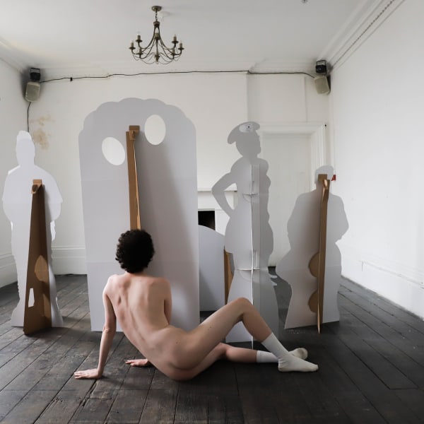 A person wearing only socks lying on their side behind some cardboard cutouts