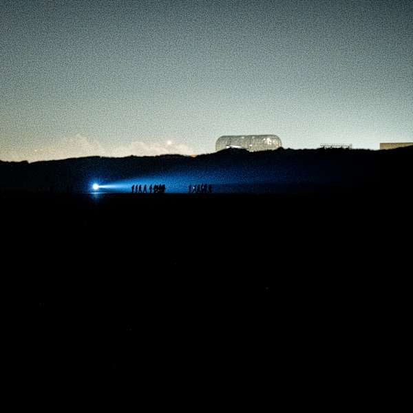 A photo of a landscape at dusk with human figures walking in silhouette, next to water under a strong outdoor torchlight 