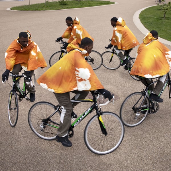 Five black male cyclists wearing orange hoodies.