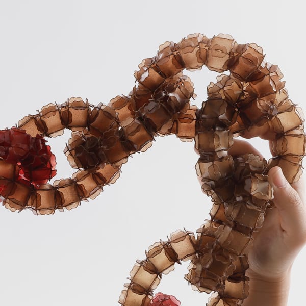 Two hands holding up a red-coloured interlinked piece of jewellery.