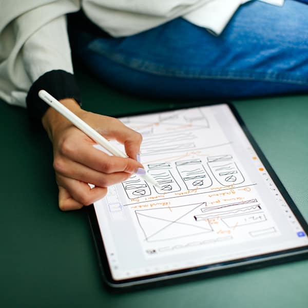 Photograph of someone taking notes on an ipad, against a green sofa.