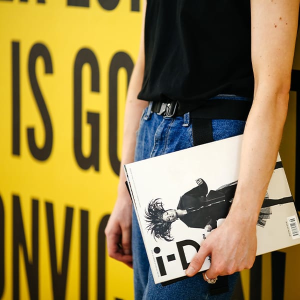 Zoomed into the lower half of a person and a hand holding a fashion book