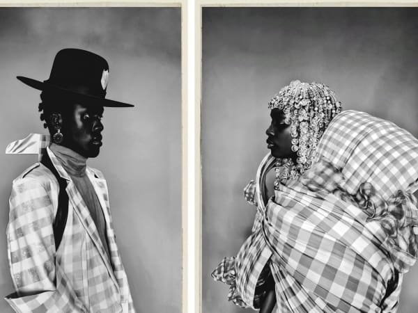 A person wearing a hat facing another person. Both are wearing garments made from a checked material. 