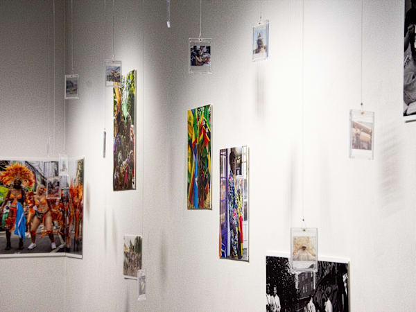 Hanging and pinned up photographic works in different sizes, orientations, colours and formats are on display in an exhibition. Overall they suggest a theme of Carnival.