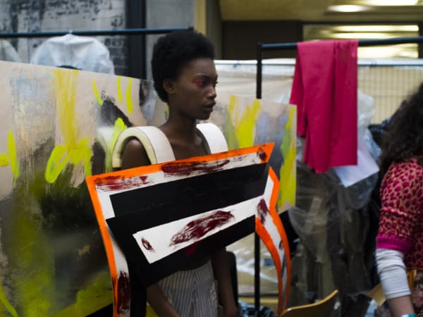 A model standing in front of a printed and painted background 