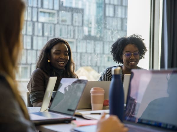 Two young women laughing and looking at their laptops