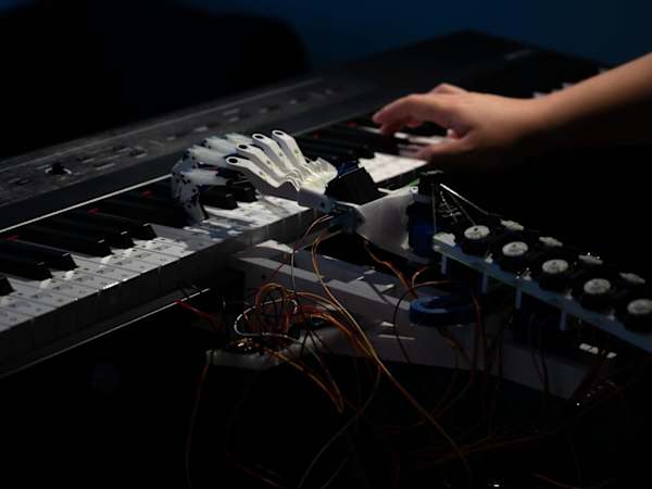 a human hand and a robot hand playing a keyboard