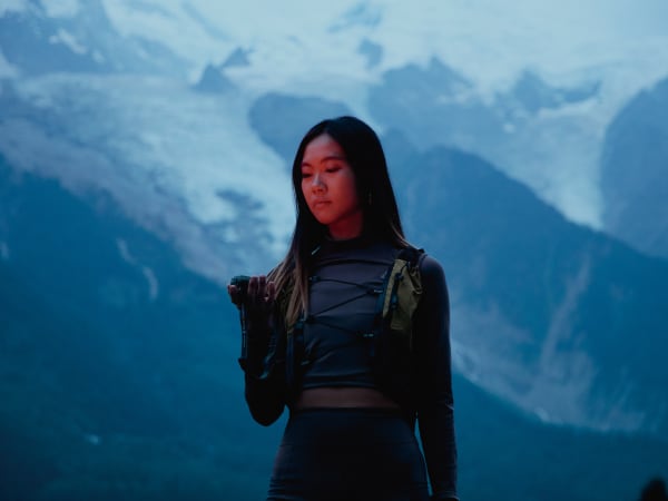 A fashion portrait with a model in dark utility clothing shot from waist up against a background with a blue gradient. 