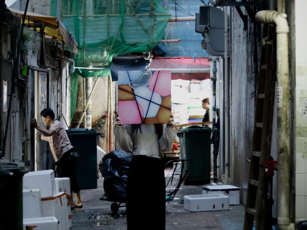 A photo pf a person holding up an artwork in front of their face against the backdrop of an outdoor market
