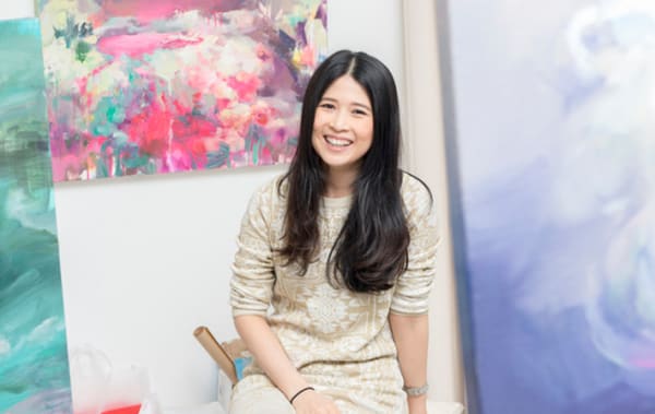 Photo of a woman sitting in front of three watercolour paintings