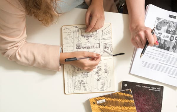 Photo of a pair of hands drawing in a sketch book using a pen