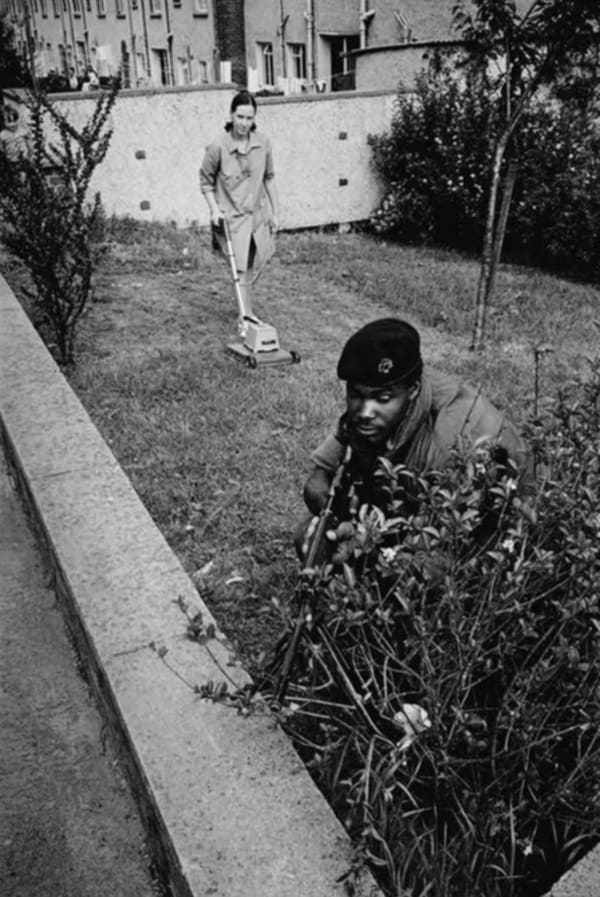 Soldier crouched in front garden as resident mows the lawn