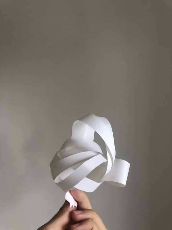 A hand holds a strip of paper twisted into an energetic 3D shape.