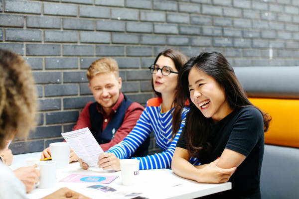 One asian female student laughing, sitting with three other students in a booth with books and papers on table
