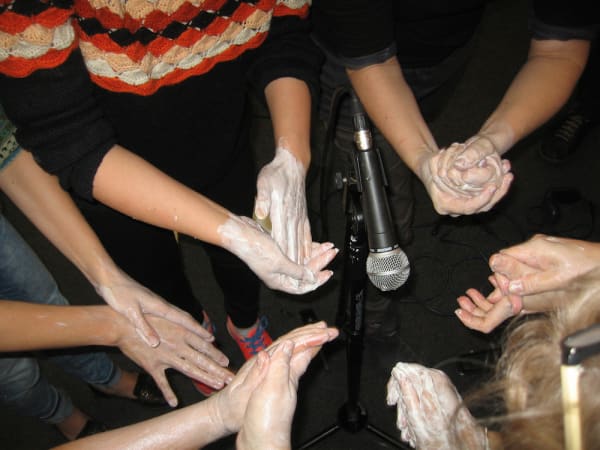 Recording sounds from hands with paste around, artists around a microphone.