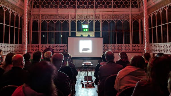 Seated audience watching a screen in an ornate space at the Horniman Museum.