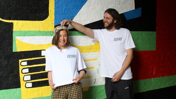 A girl and boy standing in front of a large colourful painted wall mural.