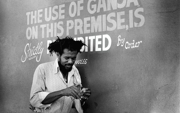 Black and white photograph of signer Glen Brown smoking in front of a handwritten no smoking sign 
