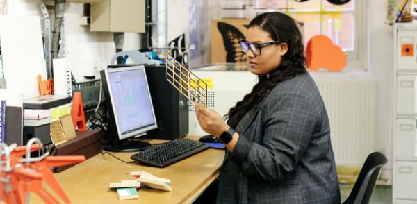 Woman looking at 3D printing and sitting at a desk.