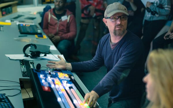 A tutor stands at a audio-visual mixing desk in order to instruct his students.