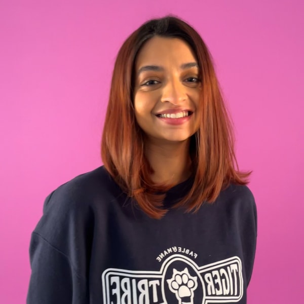 A young womanin a dark blue sweater smiles at the camera ,against a pink background