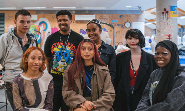Students facing the camera and smiling around a table in a fashion studio. 