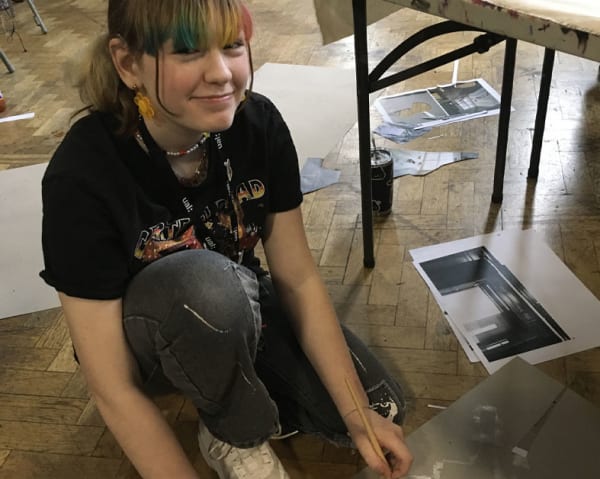 Close up of student sitting on floor smiling, she has rainbow colour dye in her fringe