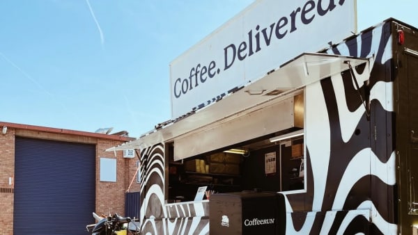 Patterned black and white coffee van with bike in front of it.