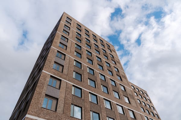 Exterior view of YourTribe Peckham, showcasing a modern tall brick building set against a backdrop of sky and clouds.
