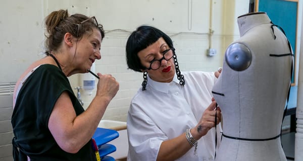 2 people adjusting fabric on a mannequin
