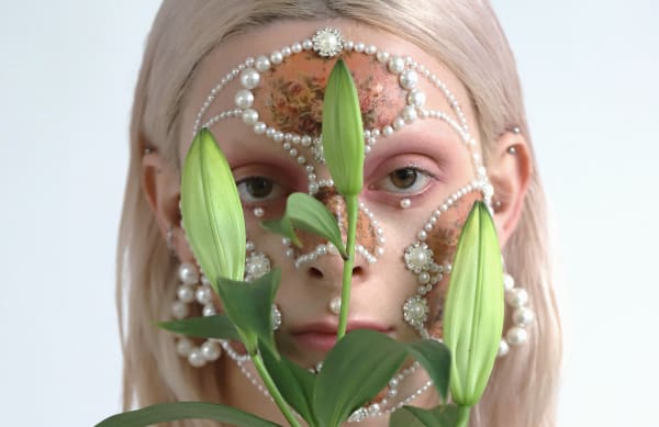 Female model with pearl facial jewellery, makeup and lilies.