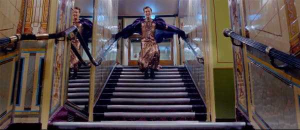 A figure leaps down a staircase within a lavish interior.