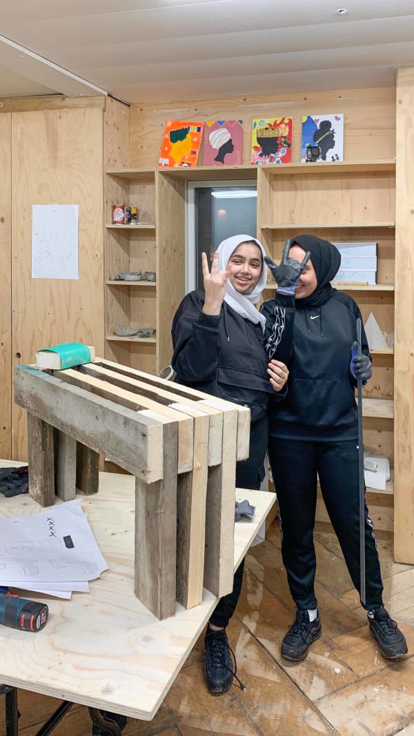 Two women standing by furniture on table, smiling and gesturing with hands