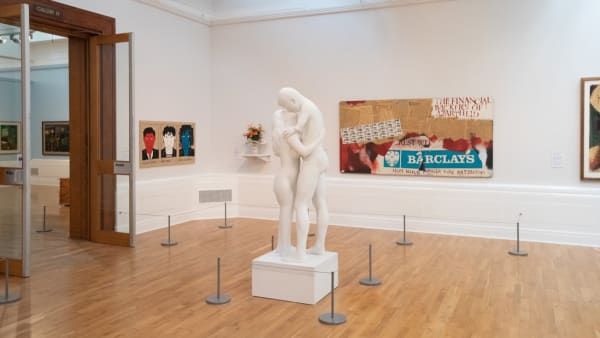 Museum room with paintings and a sculpture of 2 figures embracing.