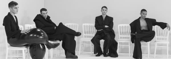 Four male models seated in loose black clothing